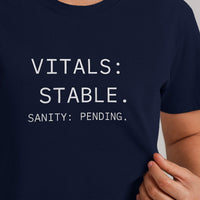 Closeup of “Vitals Stable. Sanity Pending.” text on navy t-shirt, high-contrast, readable burnout humor for nurses