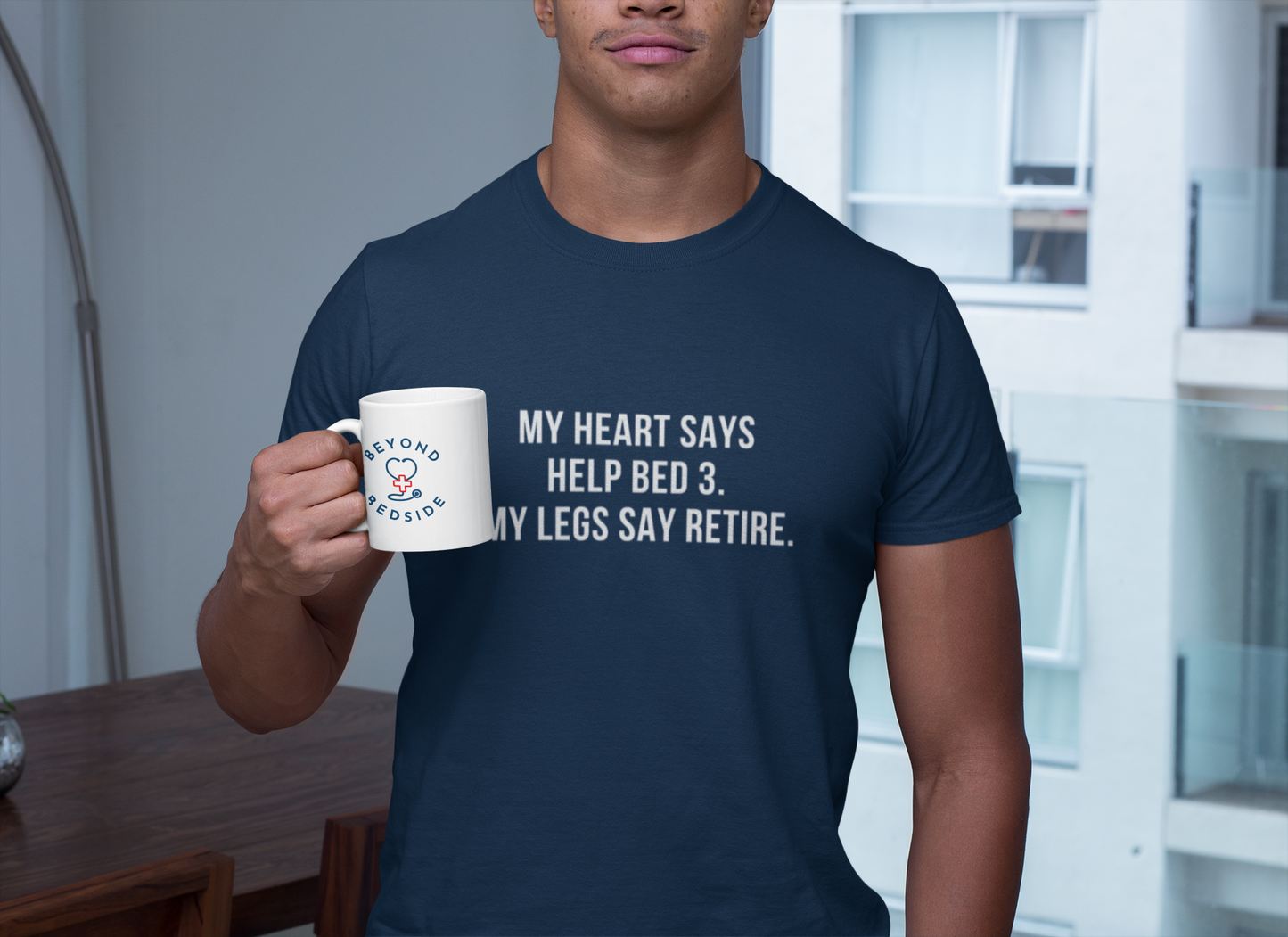 Male nurse holding coffee while wearing a t-shirt that says “My heart says help Bed 3, but my legs say retire.”
