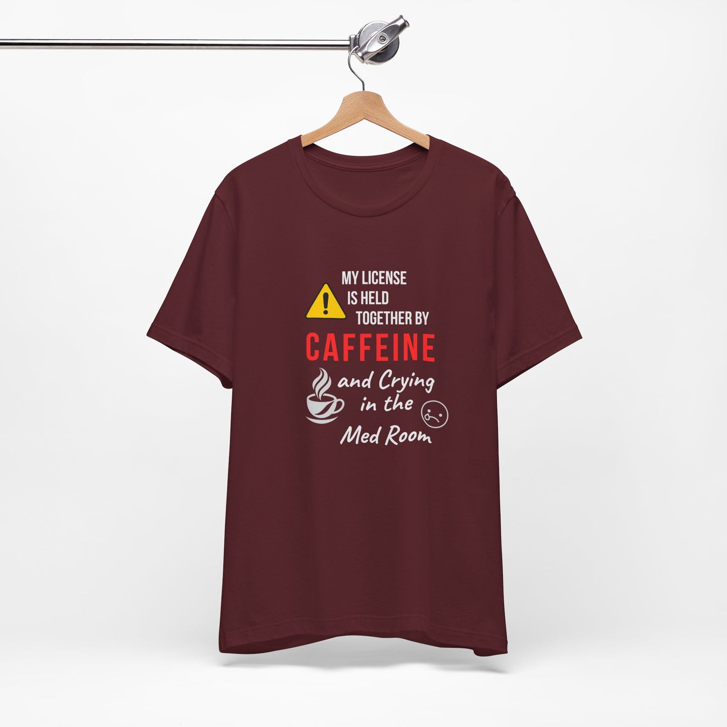Maroon “Held Together by Caffeine” shirt hanging front-facing on hanger, showing design clearly.