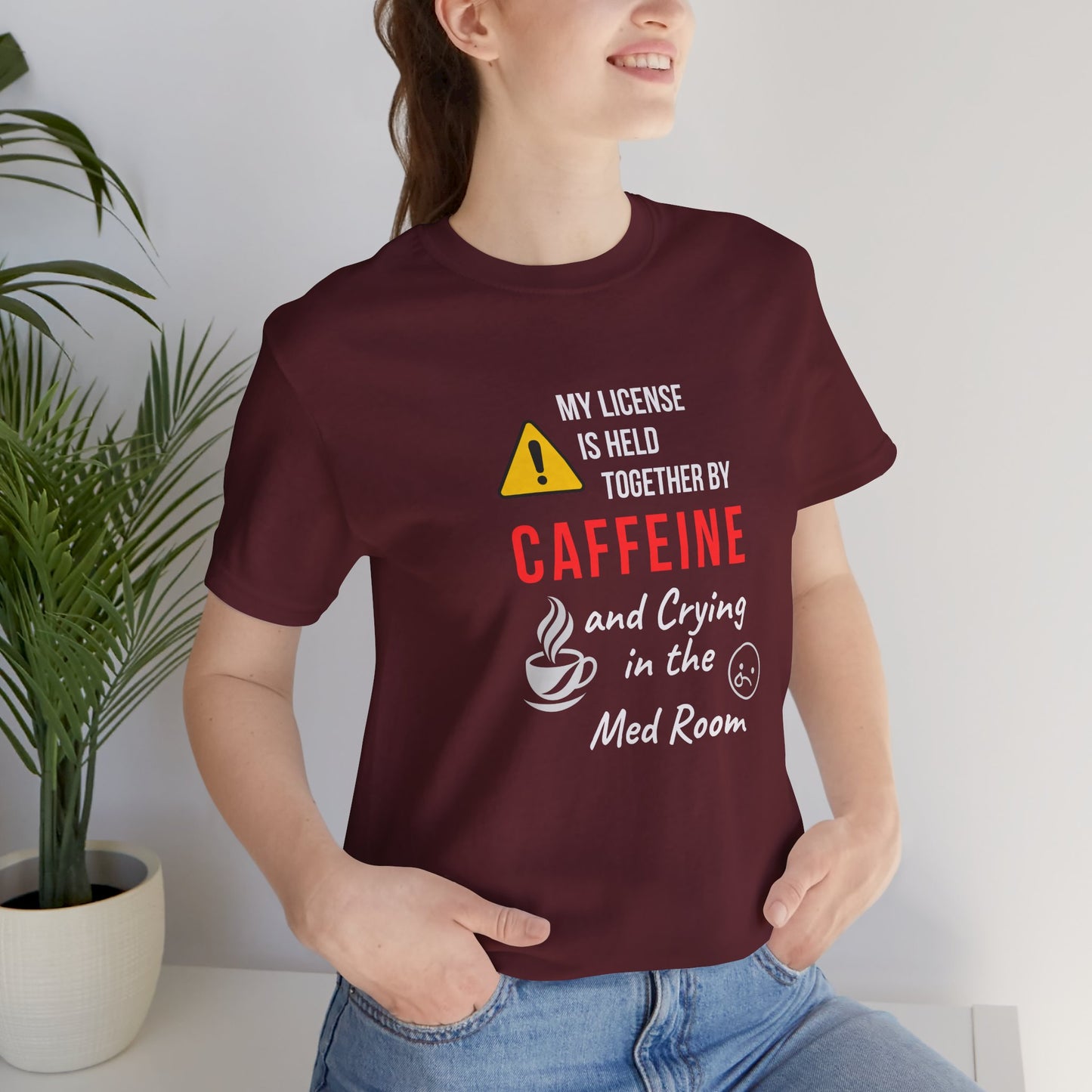 nurse at home wearing a maroon “Held Together by Caffeine” tee.