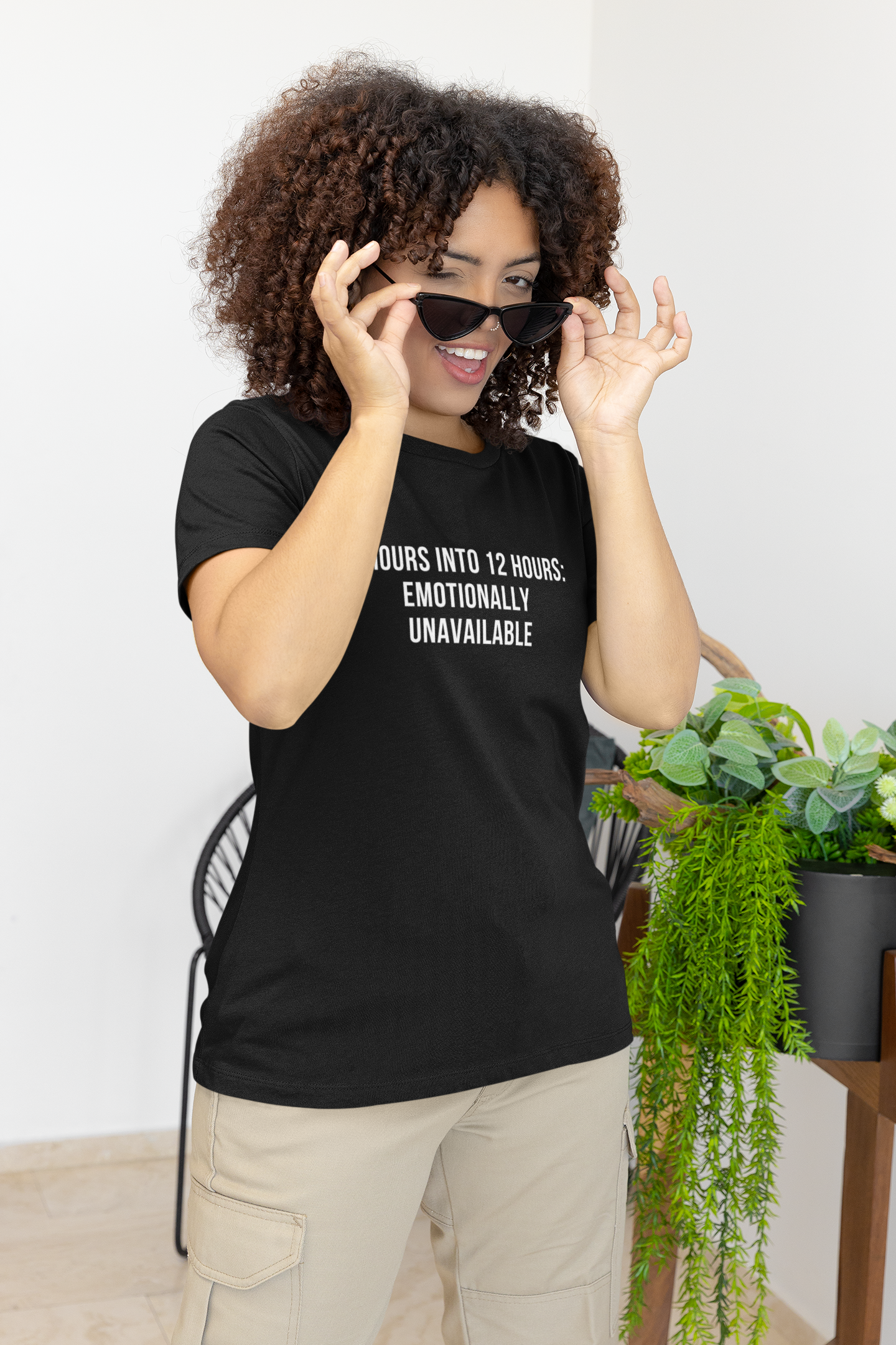 Smiling nurse in black “Emotionally Unavailable” tee with beige background.