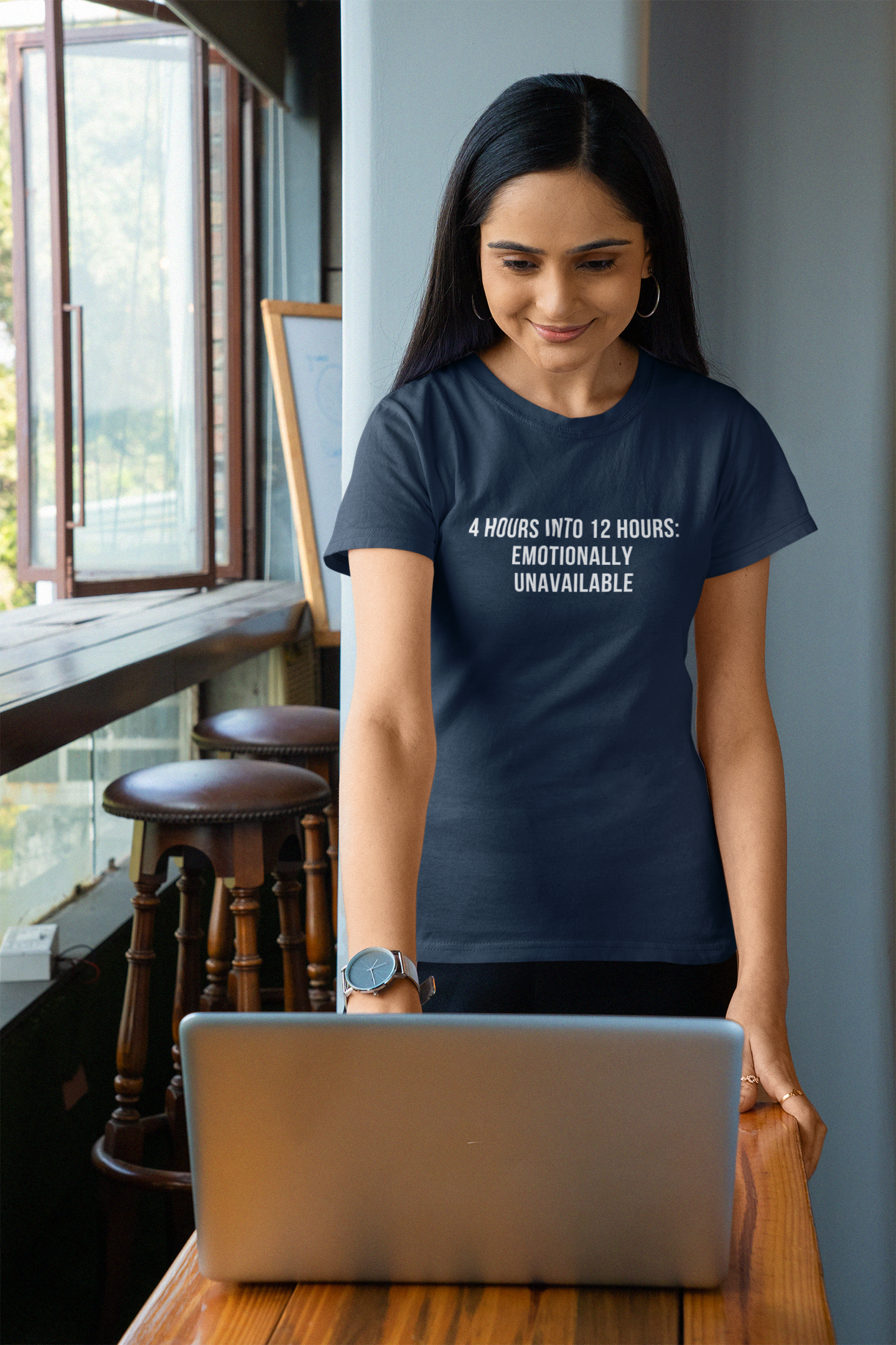 Nurse leaning on desk wearing navy burnout t-shirt that reads “Emotionally Unavailable.”
