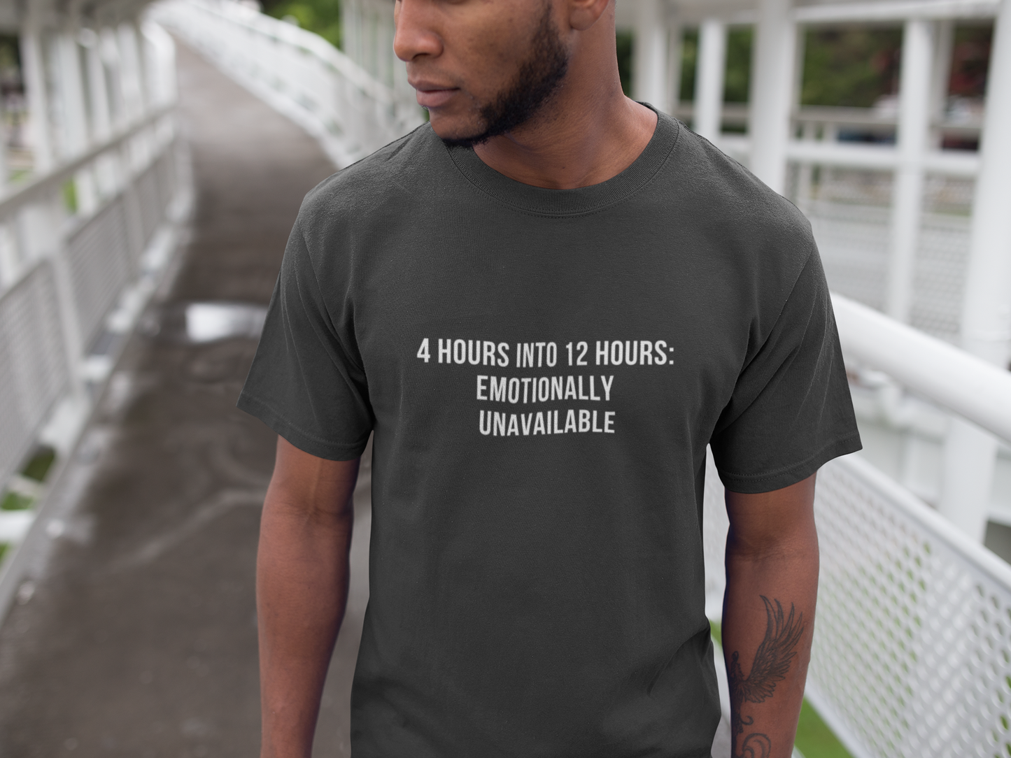 Burnout male nurse wearing gray “Emotionally Unavailable” tee sitting on couch.