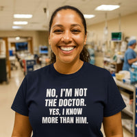 Nurse in scrubs smiling, wearing "No, I’m Not The Doctor. Yes, I Know More Than Him." shirt, hospital background.