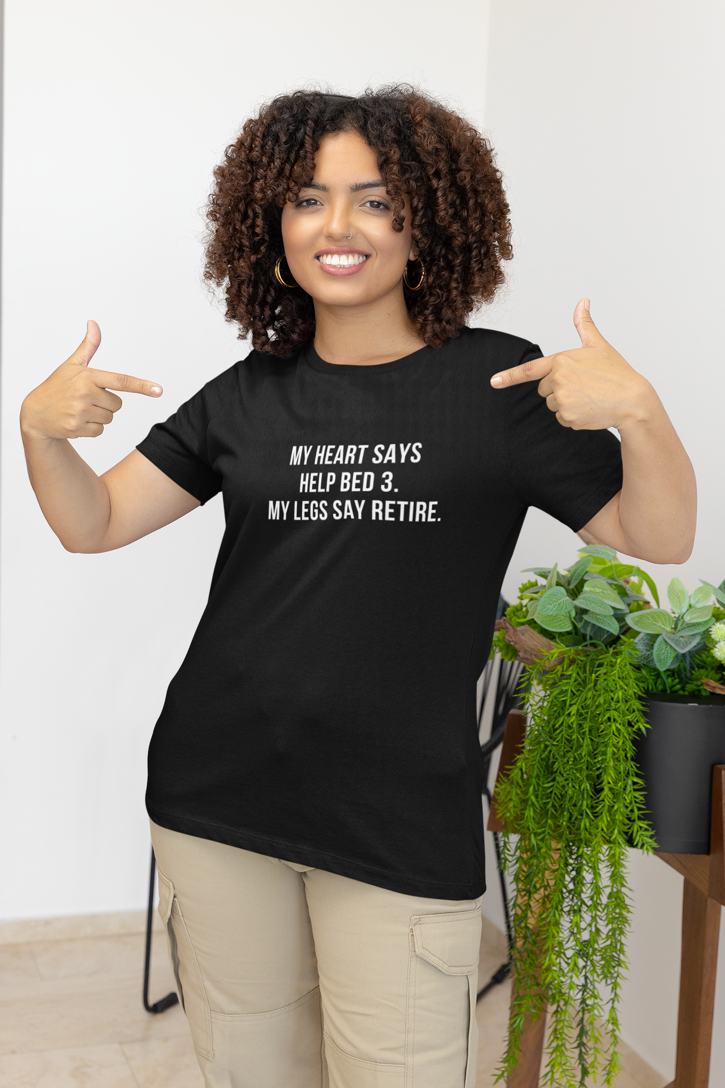 Smiling nurse pointing to her shirt with the sarcastic quote about helping Bed 3 vs. retiring.