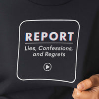 Close-up of shirt print: REPORT Lies, Confessions, and Regrets, bold white text on navy fabric.