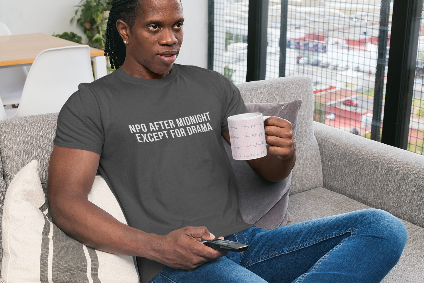 Nurse sitting down in grey burnout tee that says “NPO AFTER MIDNIGHT, EXCEPT FOR DRAMA.”