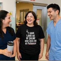 Two nurses and a male nurse in scrubs, smiling, all wearing "I Gave 1,000 ml of Saline and Zero ml of Patience" shirts, hospital hallway.
