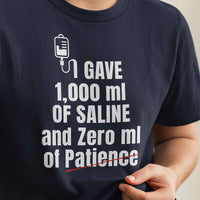 Close-up of shirt print: I Gave 1,000 ml of Saline and Zero ml of Patience, bold white text on black fabric.
