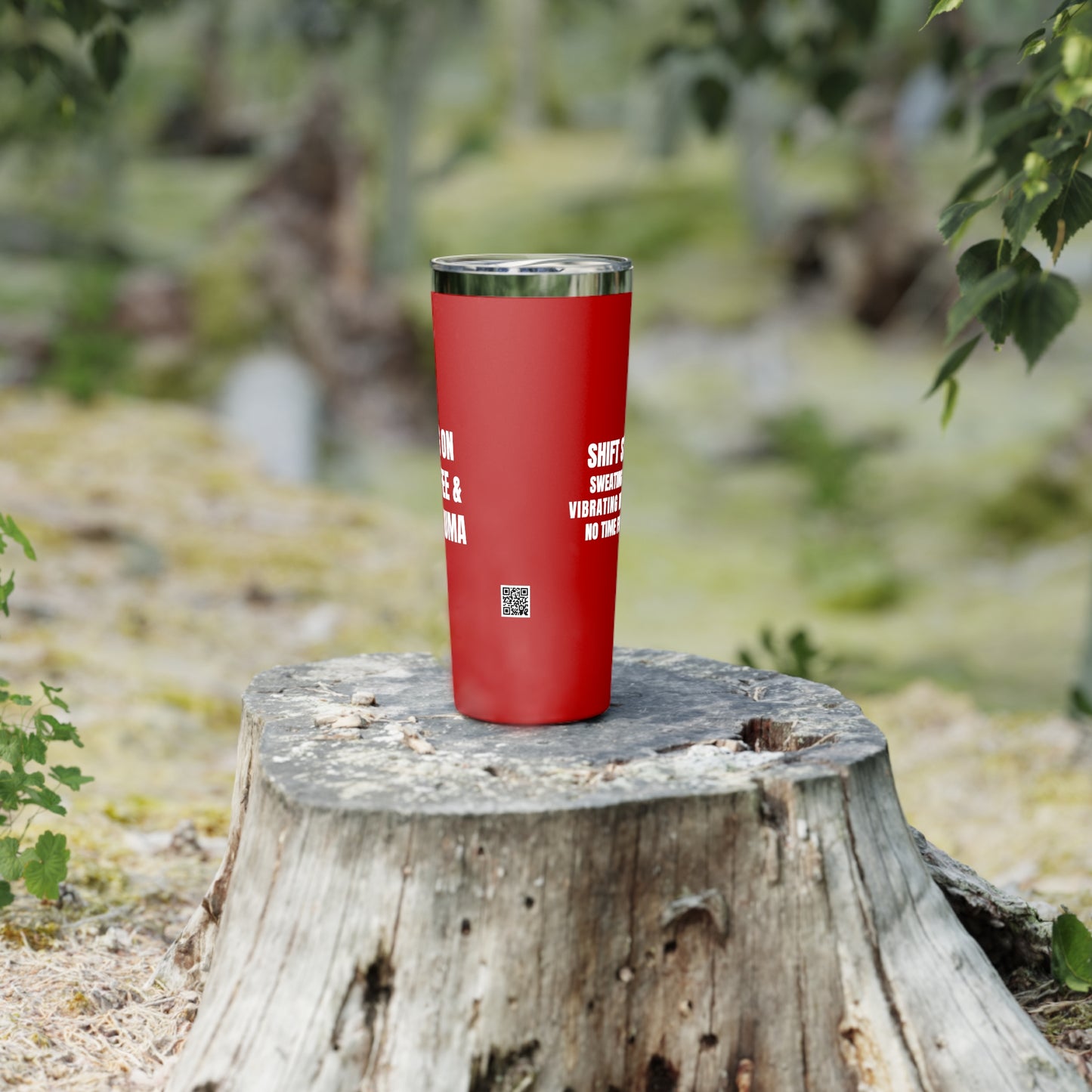 Red nurse-themed tumbler placed on a cut log in an outdoor setting, showing the text “PRN Coffee & Shift Trauma.”