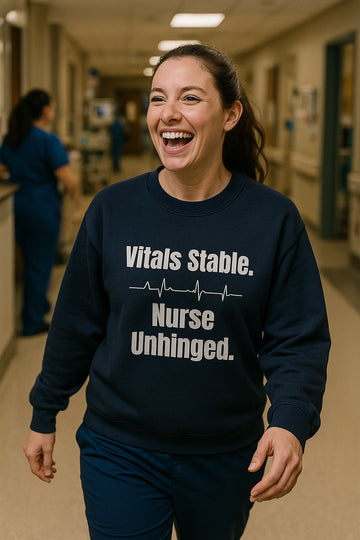Nurse walking down hospital hallway, laughing while wearing navy sweatshirt with white text “Vitals Stable. Nurse Unhinged.”
