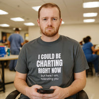 Male nurse wearing "I Could Be Charting Right Now" shirt, standing in hospital hallway.

