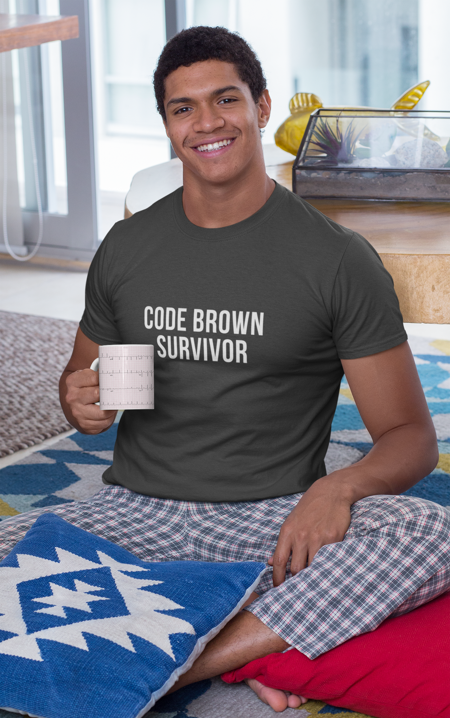 Smiling nurse in grey shirt sipping coffee; “Code Brown Survivor” text visible on chest.
