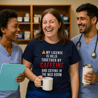 Three nurses in scrubs laughing, all wearing "My License Is Held Together By Caffeine And Crying In The Med Room" shirts, hospital background.