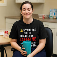 Smiling nurse in scrubs relaxin, wearing "My License Is Held Together By Caffeine And Crying In The Med Room" shirt, hospital setting.
