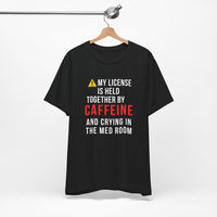 Black nurse burnout humor shirt on hanger with warning triangle and bold text: My License Is Held Together By Caffeine And Crying In The Med Room.
