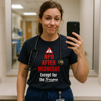 Female nurse in scrubs taking selfie, wearing "NPO After Midnight Except for the Trauma" shirt, hospital setting.
