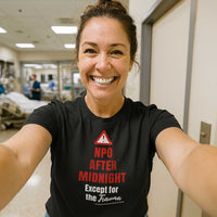 Female nurse in scrubs taking selfie, wearing "NPO After Midnight Except for the Trauma" shirt, hospital setting.
