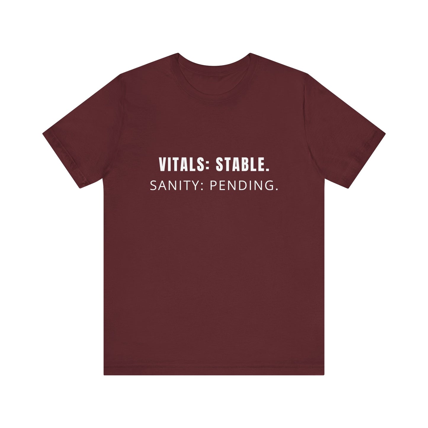 Flatlay of maroon “Vitals: Stable. Sanity: Pending.” tee on plain background.
